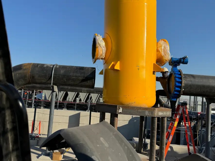 Yellow process vessel being rigged into place on a rooftop pipe rack