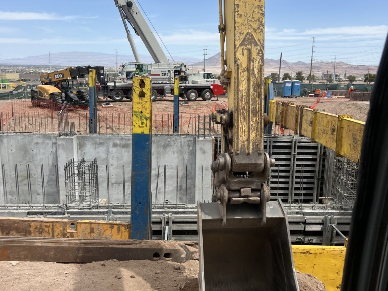 Excavator bucket with mobile crane and concrete foundation wall on an active commercial jobsite