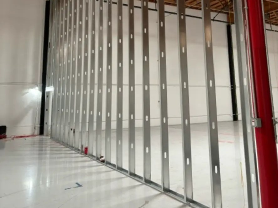 Full-height metal stud demising wall framed to the wood truss deck inside a warehouse