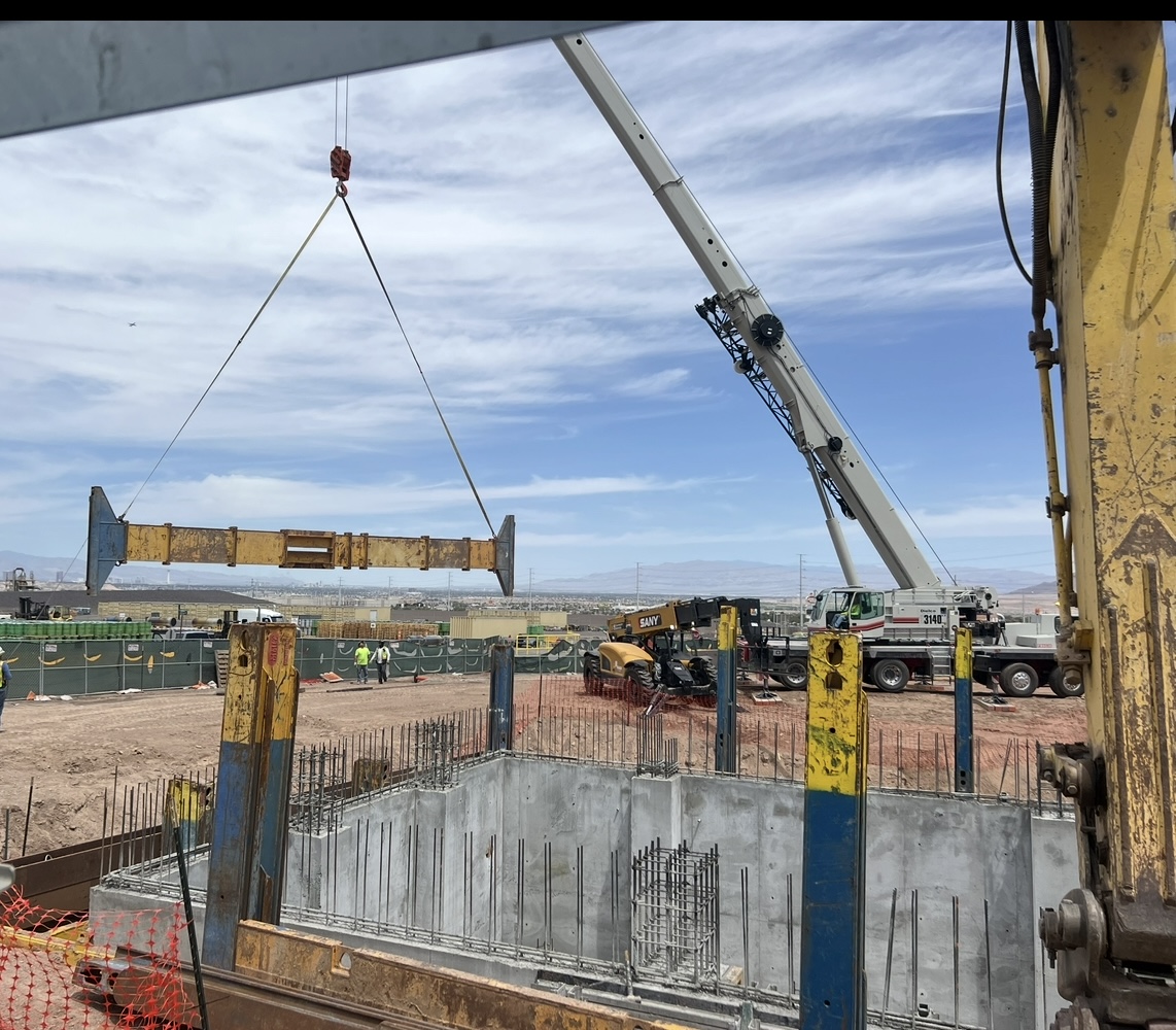 Mobile crane setting a structural steel beam over a formed concrete equipment pit